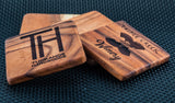 Four rectangular East Indian walnut coasters with custom engravings including a logo, winery name with grape cluster, and company text on a dark textured surface.