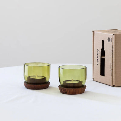 Two short Taa Candle Holders with olive green glass and dark wooden bases, side by side on a plain surface.