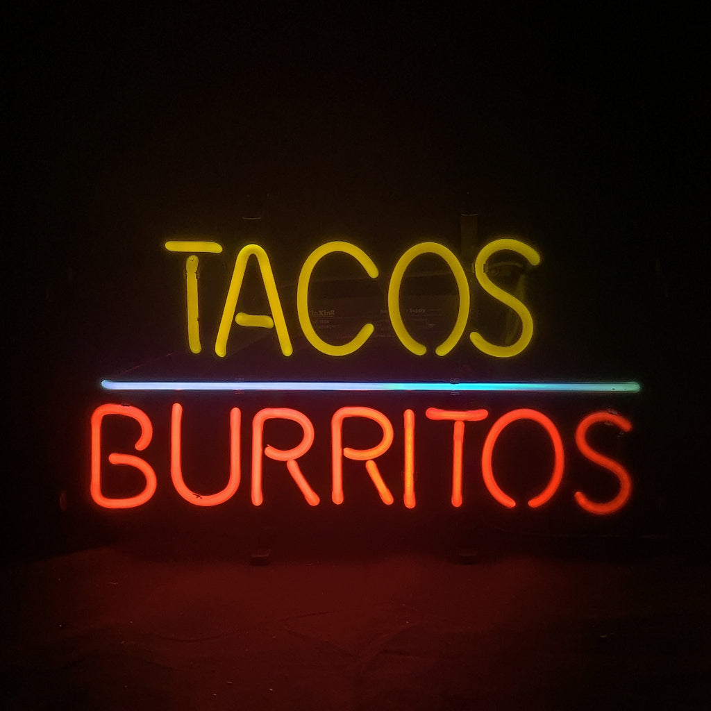 Yellow neon sign spelling 'TACOS' above a blue horizontal line and red neon 'BURRITOS' against a dark background.