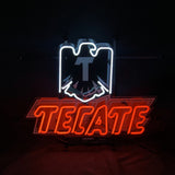 Red neon letters spelling 'TECATE' beneath a white neon outline of an eagle emblem on a black background