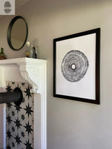 Black and white concentric tree rings print in a black frame hung on a gray wall next to white fireplace mantel with black and white star-patterned tiles.