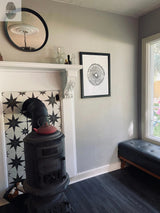 Framed black-and-white Tennessee Tree Print featuring a Paulownia Empress tree ring pattern hangs on a light gray wall above a black leather bench near a window.