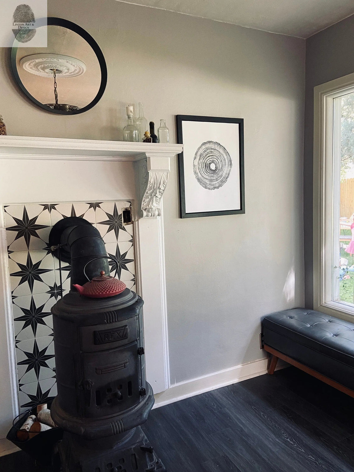 Framed black-and-white Tennessee Tree Print featuring a Paulownia Empress tree ring pattern hangs on a light gray wall above a black leather bench near a window.