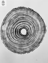 Black ink print of tree rings on white paper showing uneven, closely spaced concentric circles with textured edges around a hollow center.
