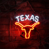 Neon sign with the word 'TEXAS' in white above a bright orange outline of a longhorn skull, mounted on a dark brick wall and hanging by a chain.