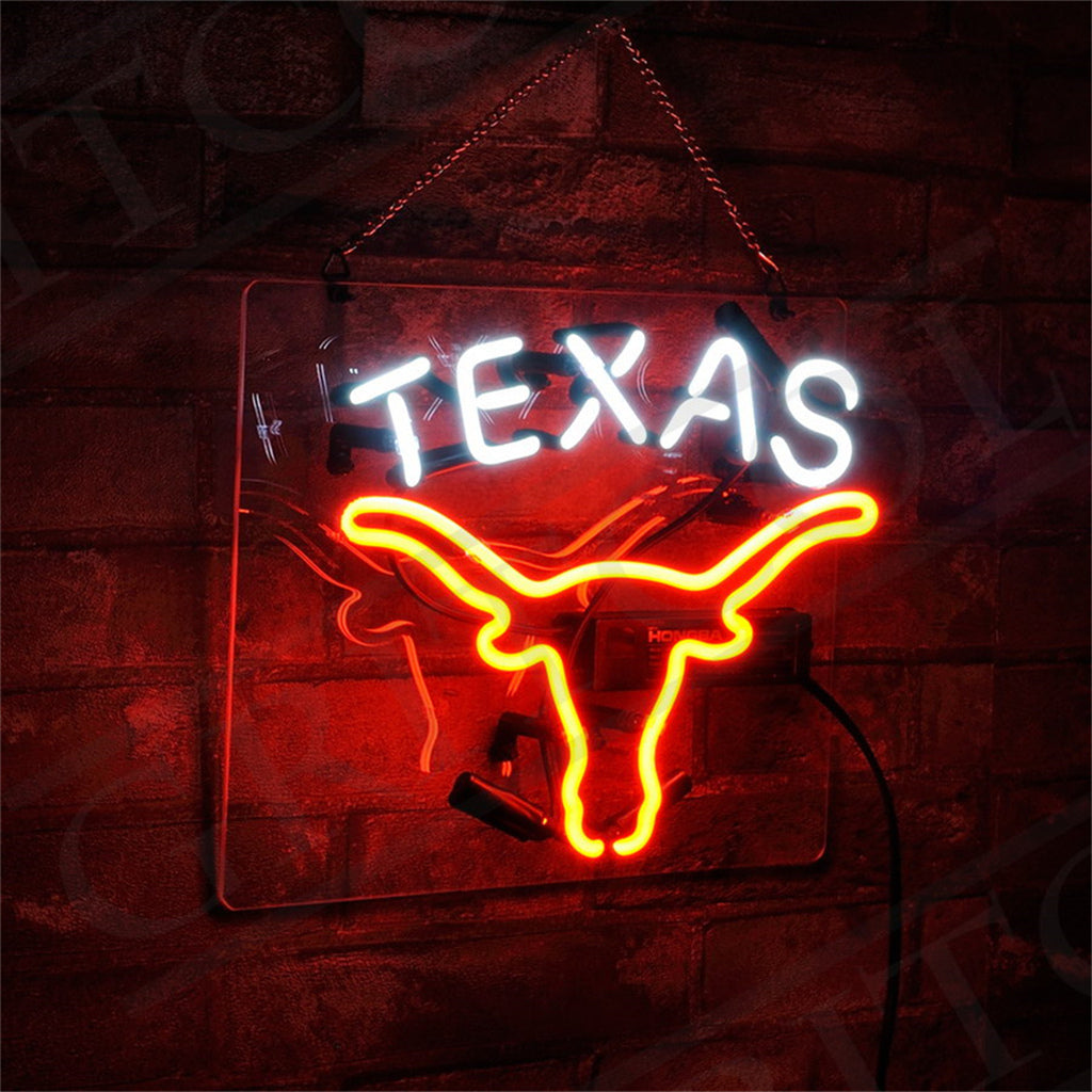 Neon sign with the word 'TEXAS' in white above a bright orange outline of a longhorn skull, mounted on a dark brick wall and hanging by a chain.