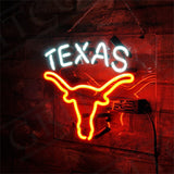 Neon sign featuring the word 'TEXAS' in white above an orange outline of a Texas longhorn skull, mounted on a brick wall.