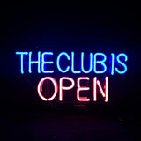 Neon sign with blue lettering 'THE CLUB IS' above pink lettering 'OPEN' on a dark background