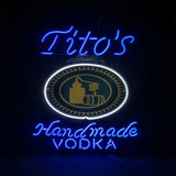 Blue neon sign with cursive 'Tito's' above a circular emblem outlined in white neon, and 'handmade VODKA' below in blue neon script.