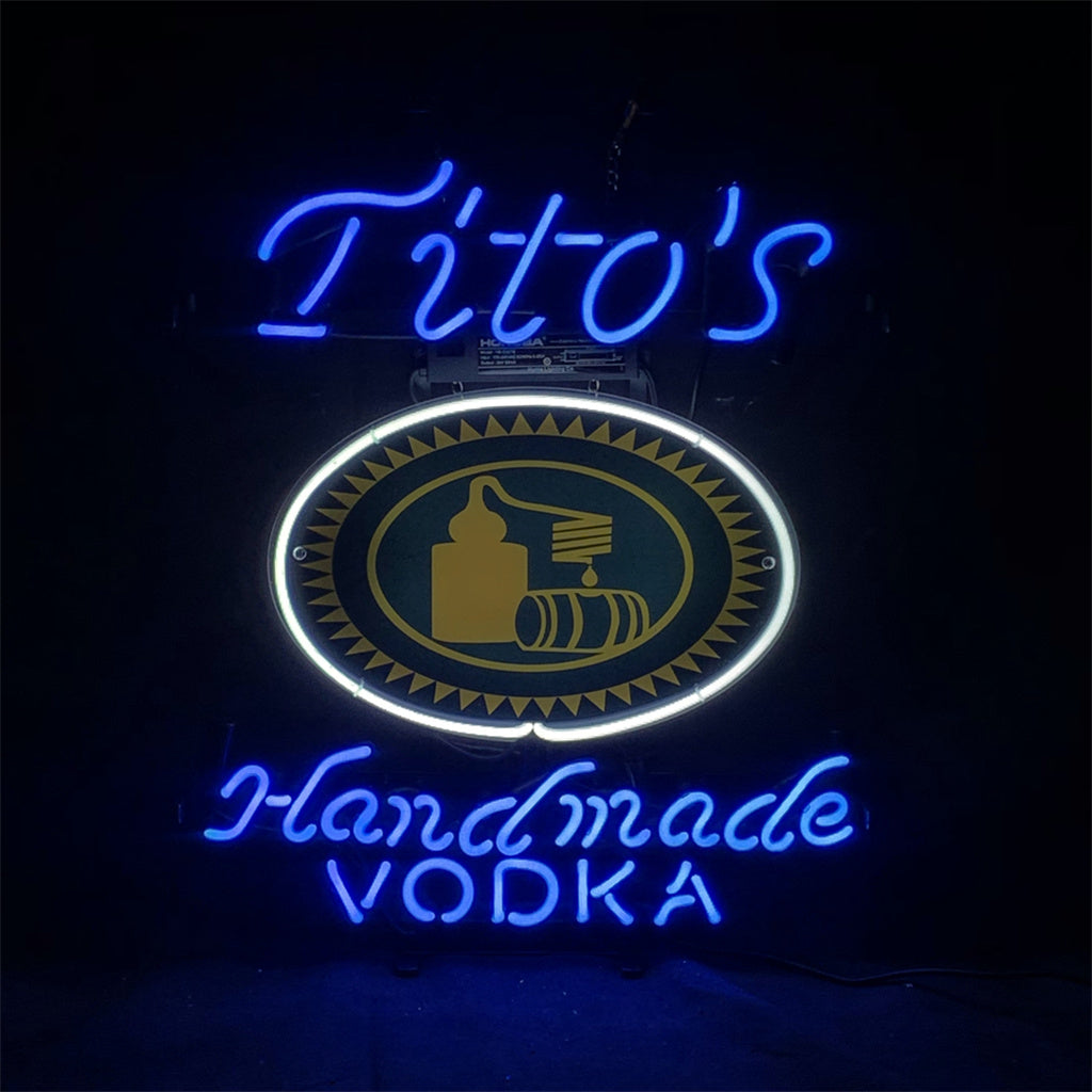 Blue neon sign with cursive 'Tito's' above a circular emblem outlined in white neon, and 'handmade VODKA' below in blue neon script.