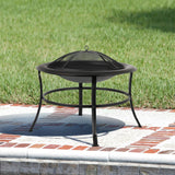 Black round metal fire pit with a mesh dome cover and curved legs, placed on a white and red brick patio with green grass background.