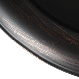Close-up of a round metal fire pit edge with a distressed black finish showing coppery rust-like streaks and subtle texture variations.