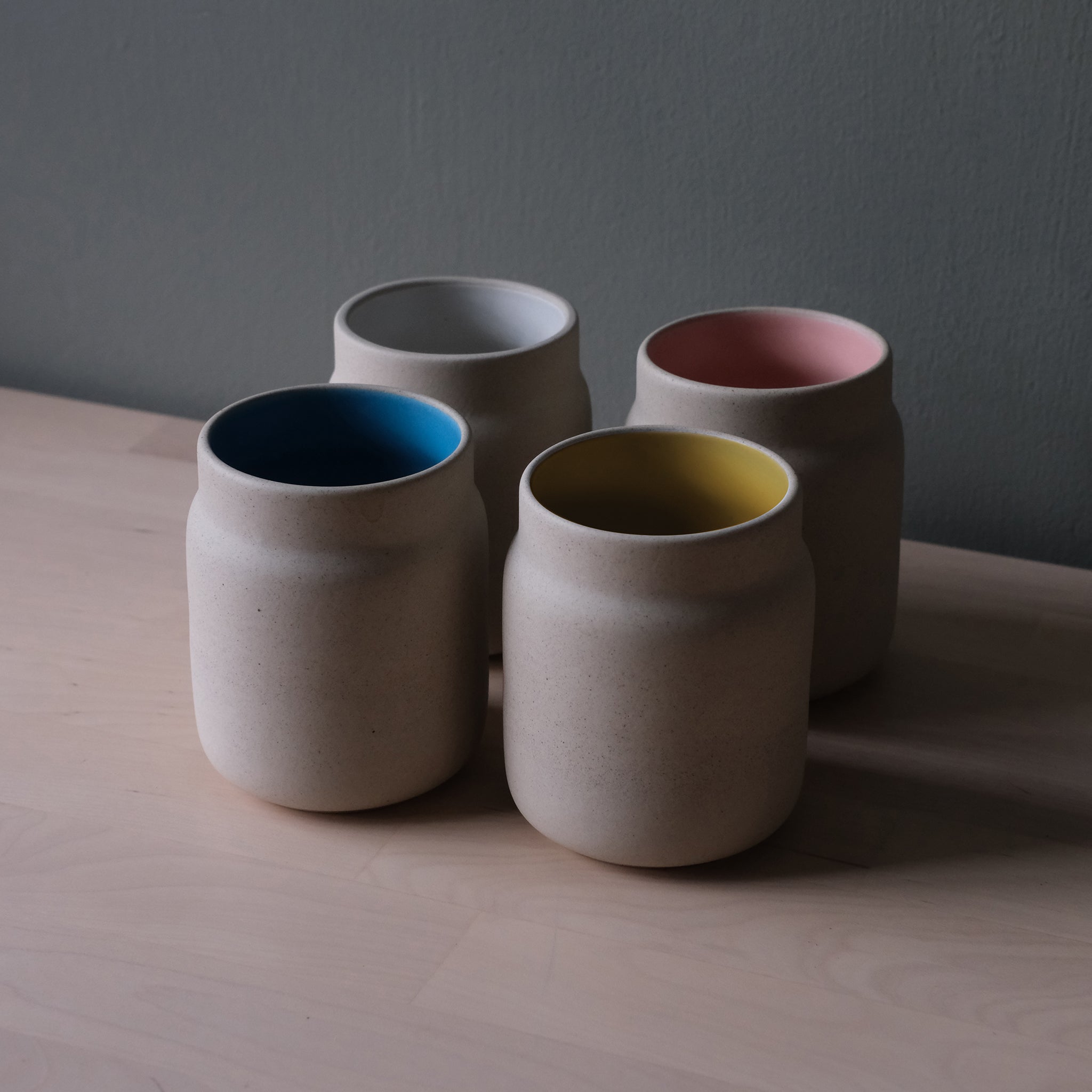 Group view of Coffee Tumbler Mugs in White Matte, Blue, Pink Matte, and Yellow colors displayed on a neutral surface