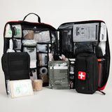 Open black and red first aid kit with organized mesh pockets holding bandages, gauze, medical tape, chest seal packs, and two black pouches, one with white cross patch.