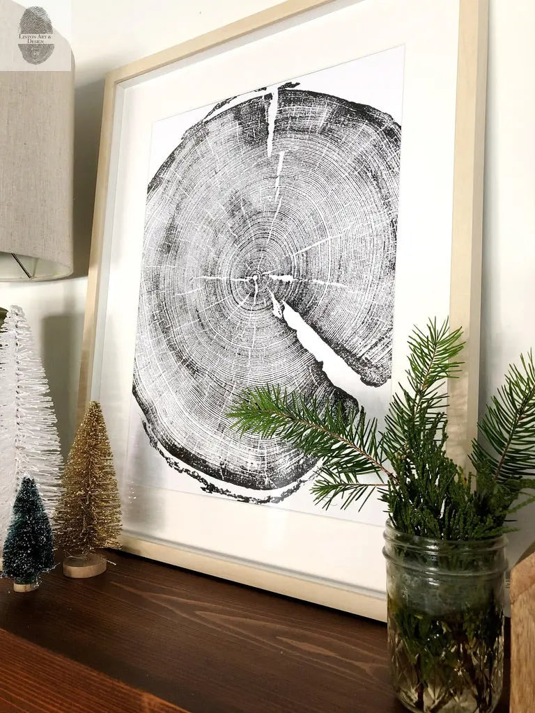 Black and white print of a detailed pine tree cross-section framed in light wood, displayed on a wooden surface with small decorative trees and a jar of green pine branches.