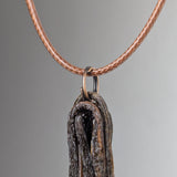 Close-up of a pendant shaped like a textured, curled dark brown and black natural element, hanging from a light brown braided cord necklace.