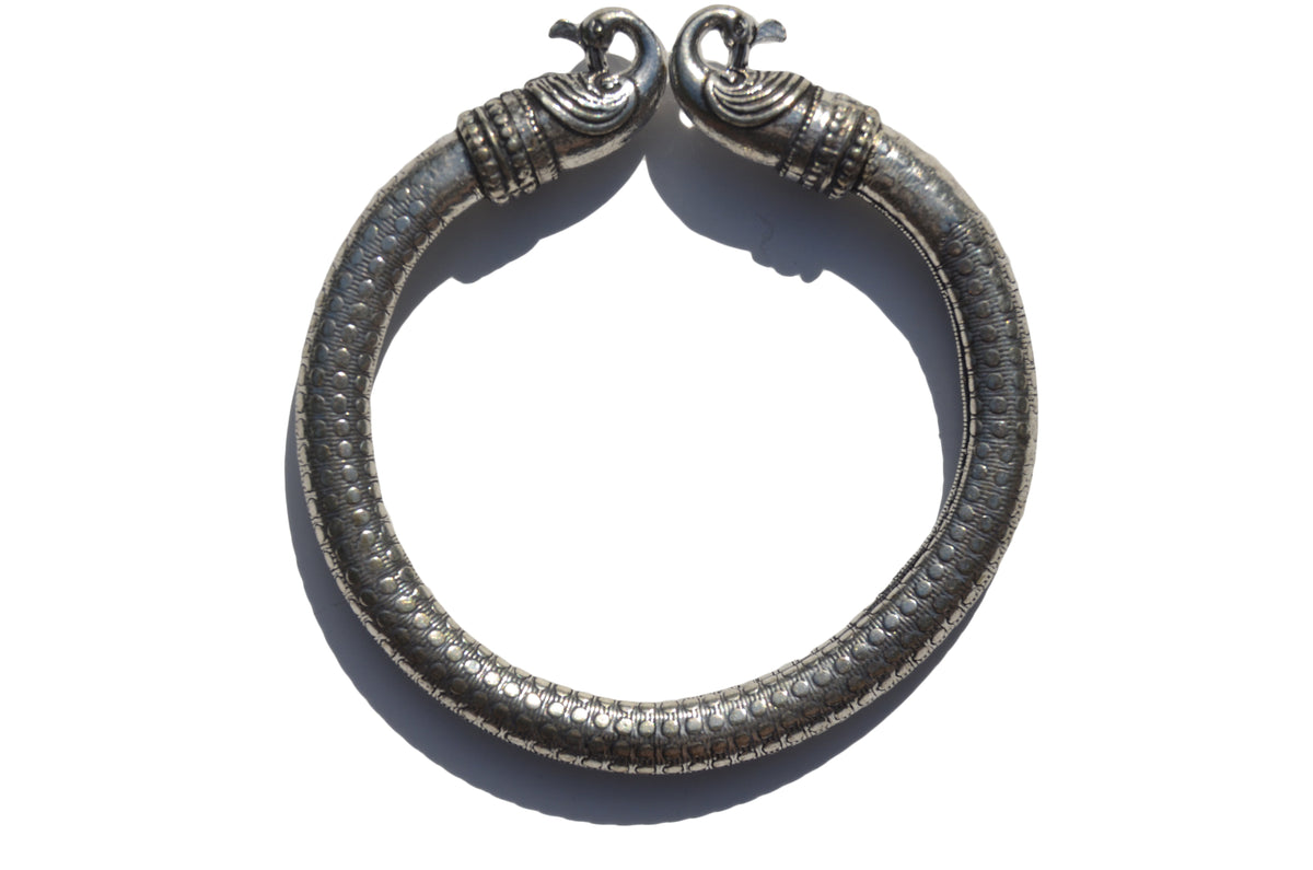 Antique Norse Viking bracelet with two detailed peacock heads facing each other and a dotted pattern along the thick metal band, shown from above.