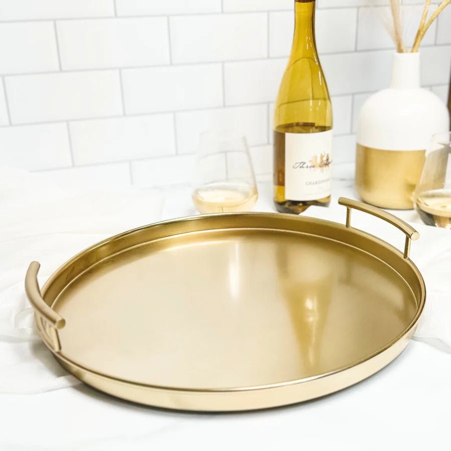 Gold metal round tray on a table with wine bottle and glasses in the background