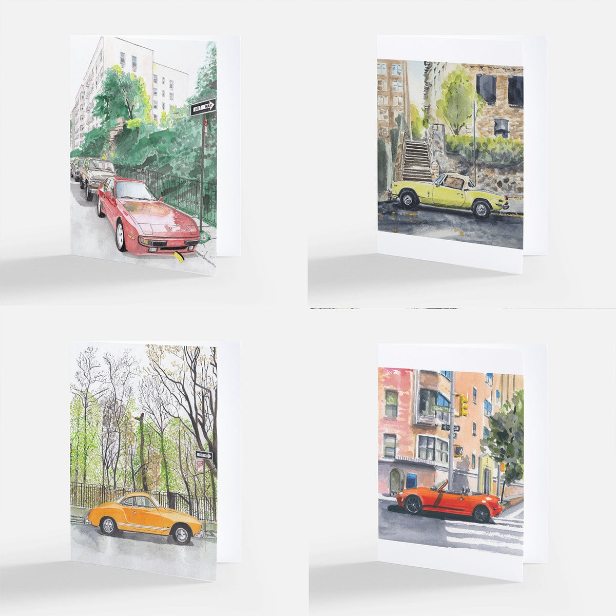 Four folded note cards each showing a watercolor illustration of classic cars—red, yellow, orange, and red—parked or driving in urban street scenes with buildings, trees, and stairs.