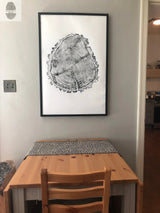 Black and white close-up tree ring print in a black frame mounted on a light gray wall above a small wooden table with a patterned runner and a wooden chair.