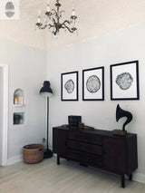 Minimalist room corner with dark wood sideboard displaying a vintage gramophone and decor, three monochrome circular prints on white walls, and a chandelier overhead.