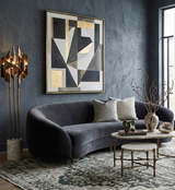 Curved dark grey velvet sofa with dove grey and beige textured pillows, set against a blue-grey textured wall featuring large abstract art in black and gold.