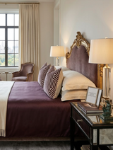 Bedroom with a velvet-upholstered headboard in rich plum, complemented by matching plum bedspread and geometric-patterned throw pillows in dark and light tones.
