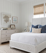 Bedroom with white woven headboard and bed frame, white bedding accented by navy blue velvet pillows with bold chevron patterns, and beige lumbar pillow.