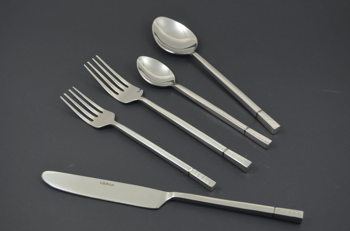 Five-piece stainless steel flatware set including a knife, two forks, a tablespoon, and a teaspoon with square-patterned handles on a dark background.