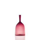 Smooth glass bottle with a wide rounded base transitioning from dark magenta at the neck to lighter pink towards the bottom, shown upright on a reflective surface.