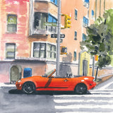 Red convertible sports car parked at a crosswalk in front of peach and beige urban buildings with shadows cast on the street and a leafy green tree on the right.