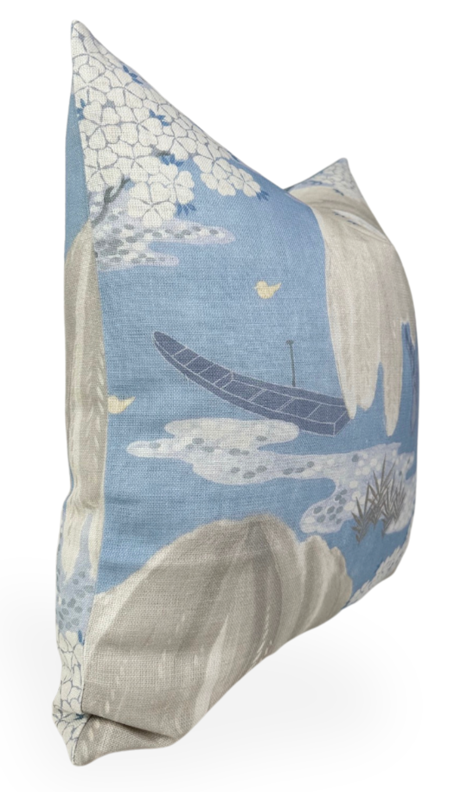 Square pillow with a soft blue background featuring a dark boat, white floral clusters, cream-colored rocks, and small yellow birds in a stylized natural scene.