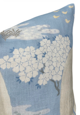 Pillow cover in soft blue featuring white flowering tree branches and small yellow bird silhouettes near the top corner against a textured fabric background.