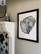 Black and white framed print of cross-sectioned cedar tree rings, hanging on a light gray wall above a white mantel with decorative molding and bottles.