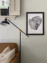 Black-framed print of a black-and-white cedar tree cross-section with growth rings, mounted on a light gray wall above a brown leather sofa and next to a black floor lamp.