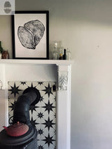 Black and white star-patterned tile behind a black cast iron wood stove with a red teapot, white decorative fireplace mantel, and framed black and white wood cross-section print above.
