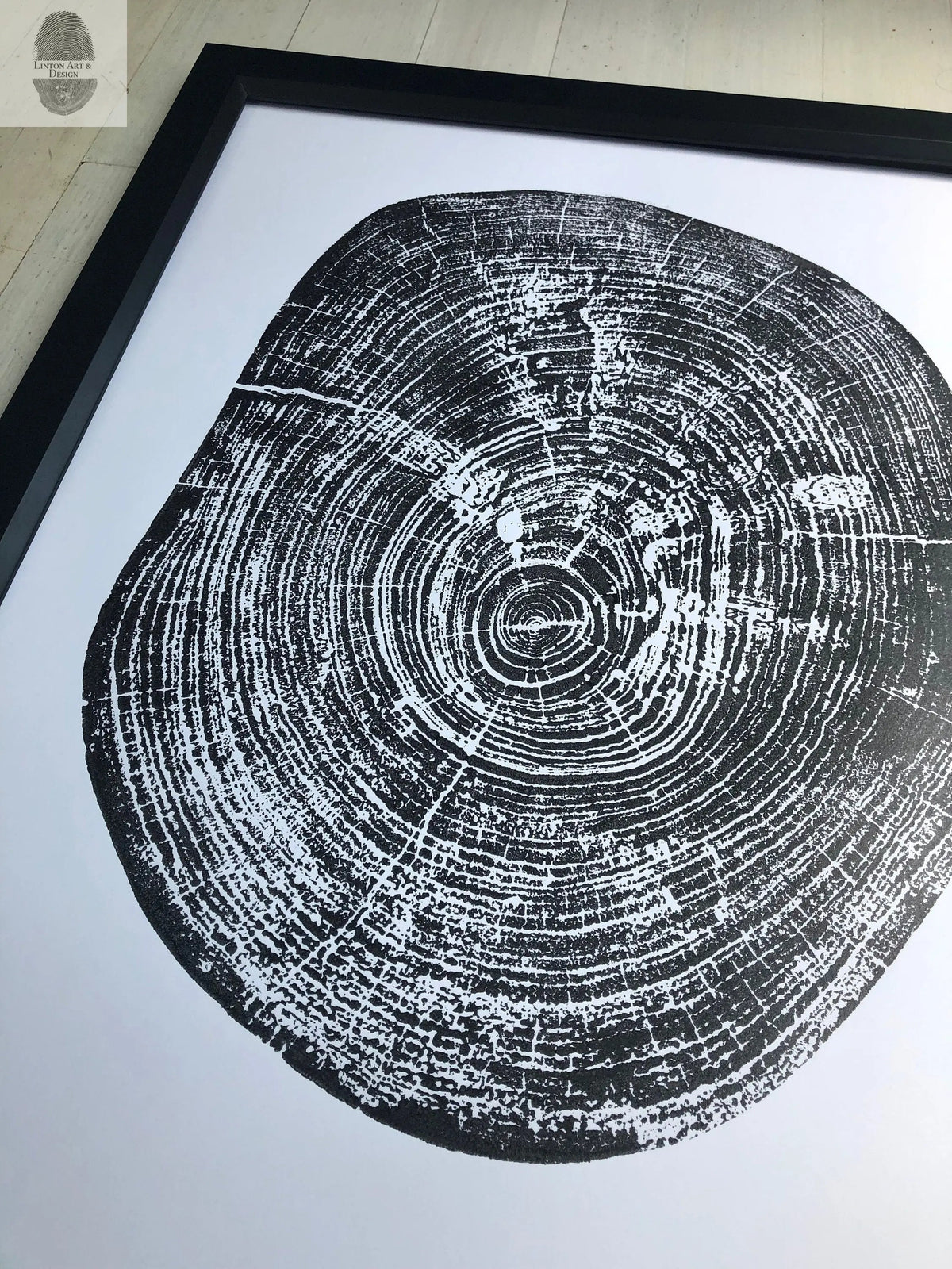 Black and white print of a pecan tree cross-section showing detailed annual rings and cracks, framed in black wood against a light floor.