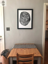 Black and white print of a pecan tree cross-section with growth rings, framed in black and hung on a light gray wall above a small wood table with chairs.