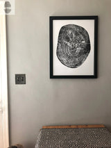 Black and white print of a pecan tree cross-section with detailed growth rings, framed in black and hung on a light gray wall above a patterned black and white tablecloth.
