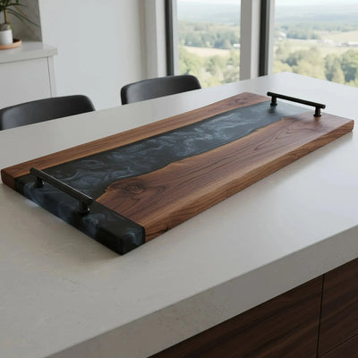 Live edge black walnut charcuterie board with smoky black epoxy resin river and matte black cylindrical handles, handcrafted and sealed with food-safe oil.