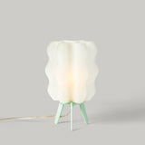 White translucent wavy lamp shade on a pastel mint green tripod base with a cord extending to the left, set against a neutral light gray background.