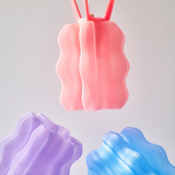 Three wavy lamps in pink, purple, and blue, each with vertical ridges and a soft translucent finish, suspended against a pale background.