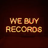Orange neon light sign with the words 'WE BUY RECORDS' against a dark background