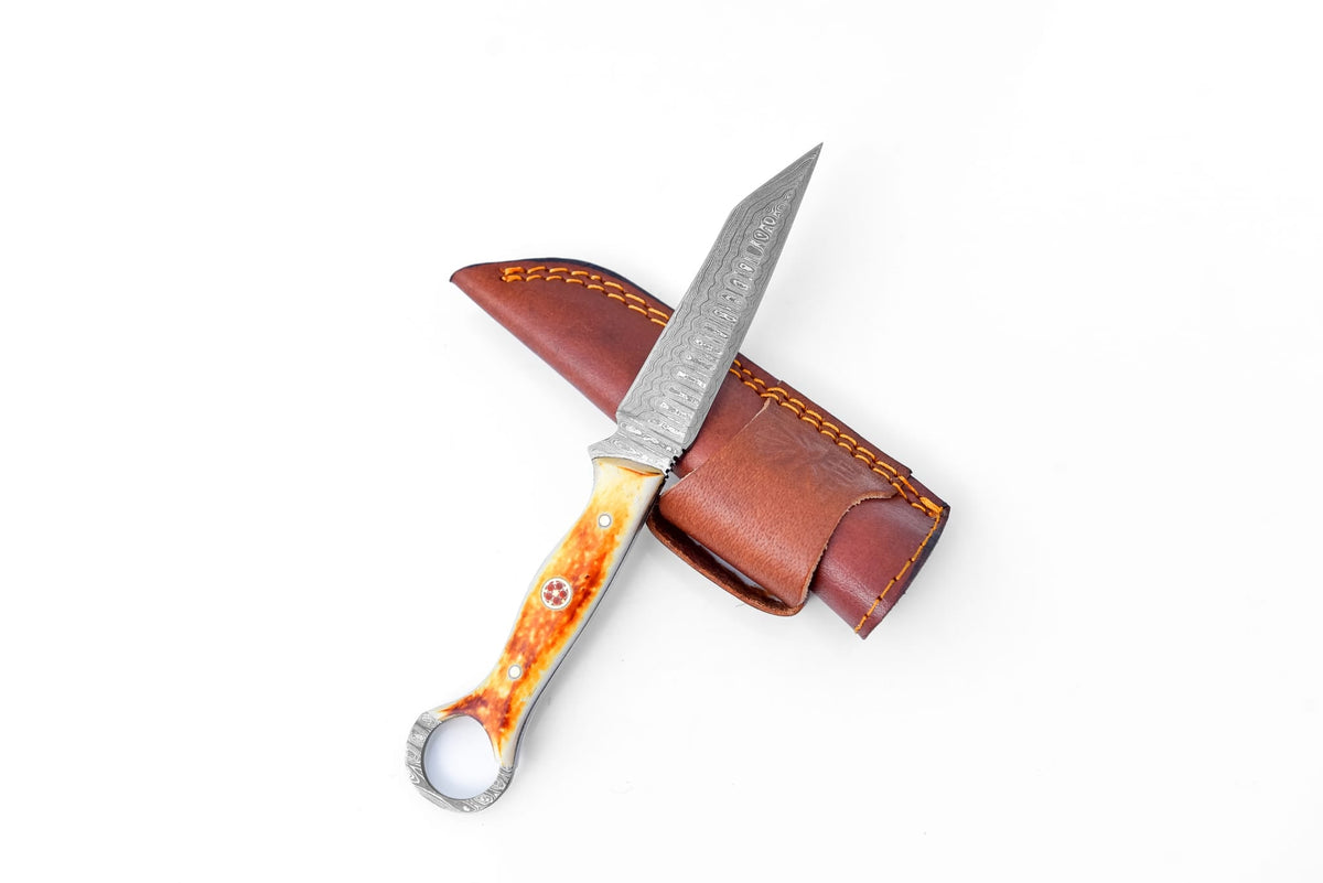 Sundancer Burnt Bone Utility Blade TK-217 knife with amber-hued handle and patterned Damascus steel blade resting beside a leather sheath.