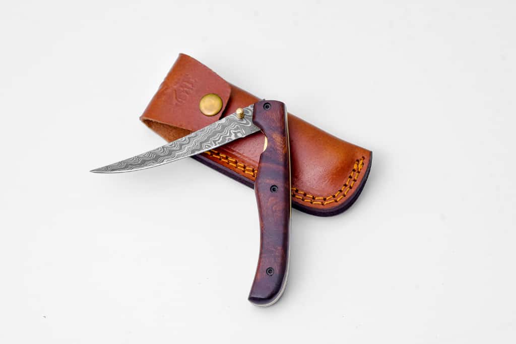 Fish fillet folding knife - TF-095 with Damascus steel blade and rose wood handle resting beside its leather sheath.