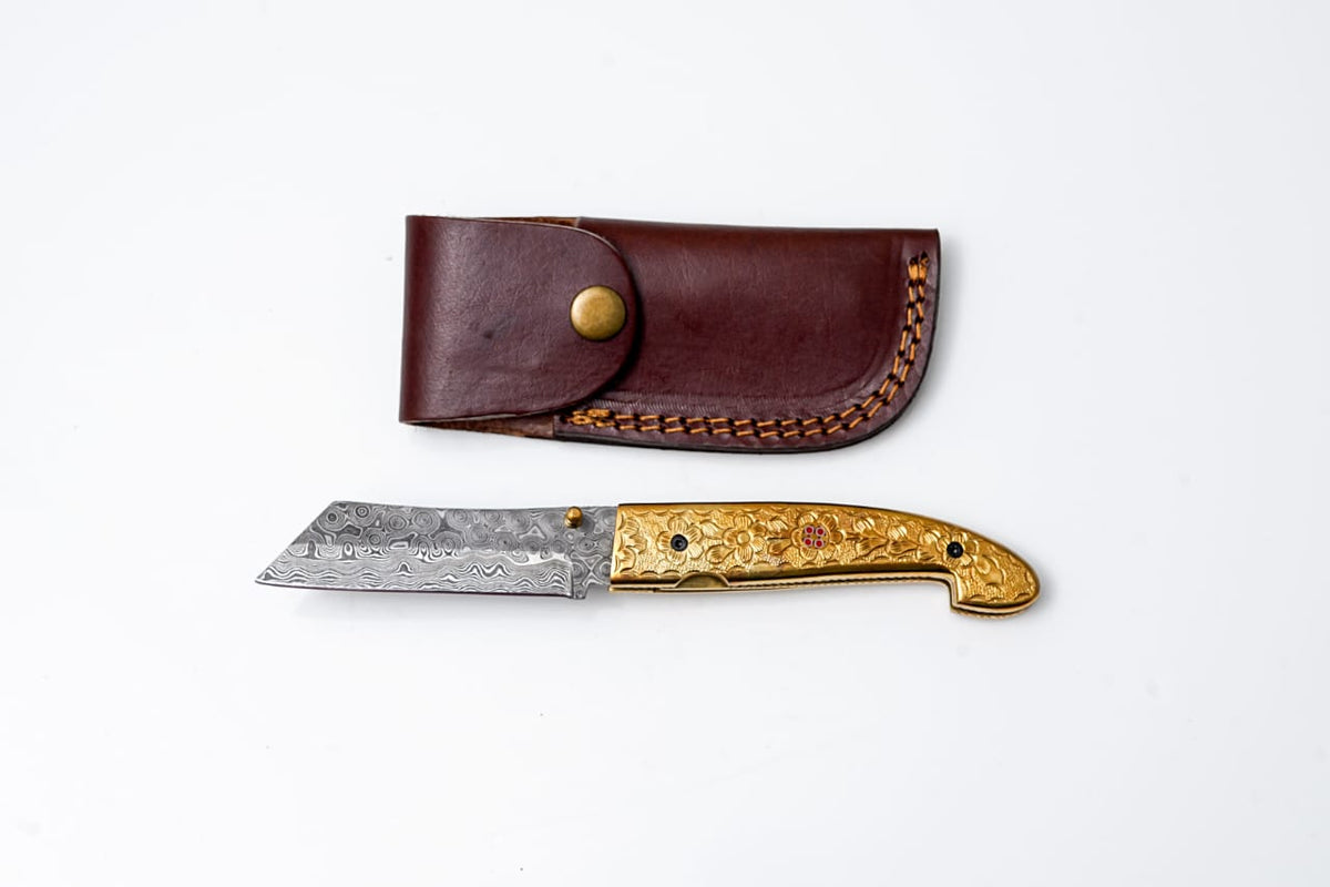 B.
Titan Golden Eagle Pocket Knife displaying engraved brass handle and Raindrop Damascus folding blade