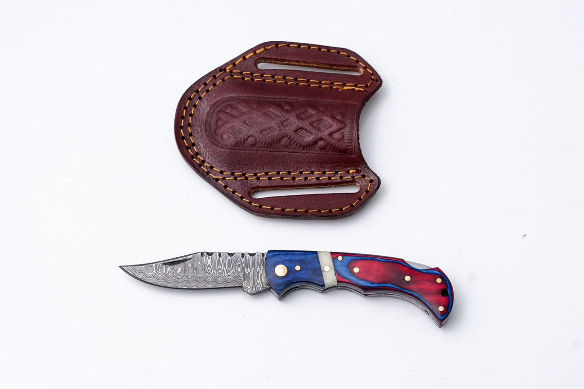 Patriot Series Damascus Folding Knife with red and blue pakkawood handle laid next to hand-stitched leather sheath