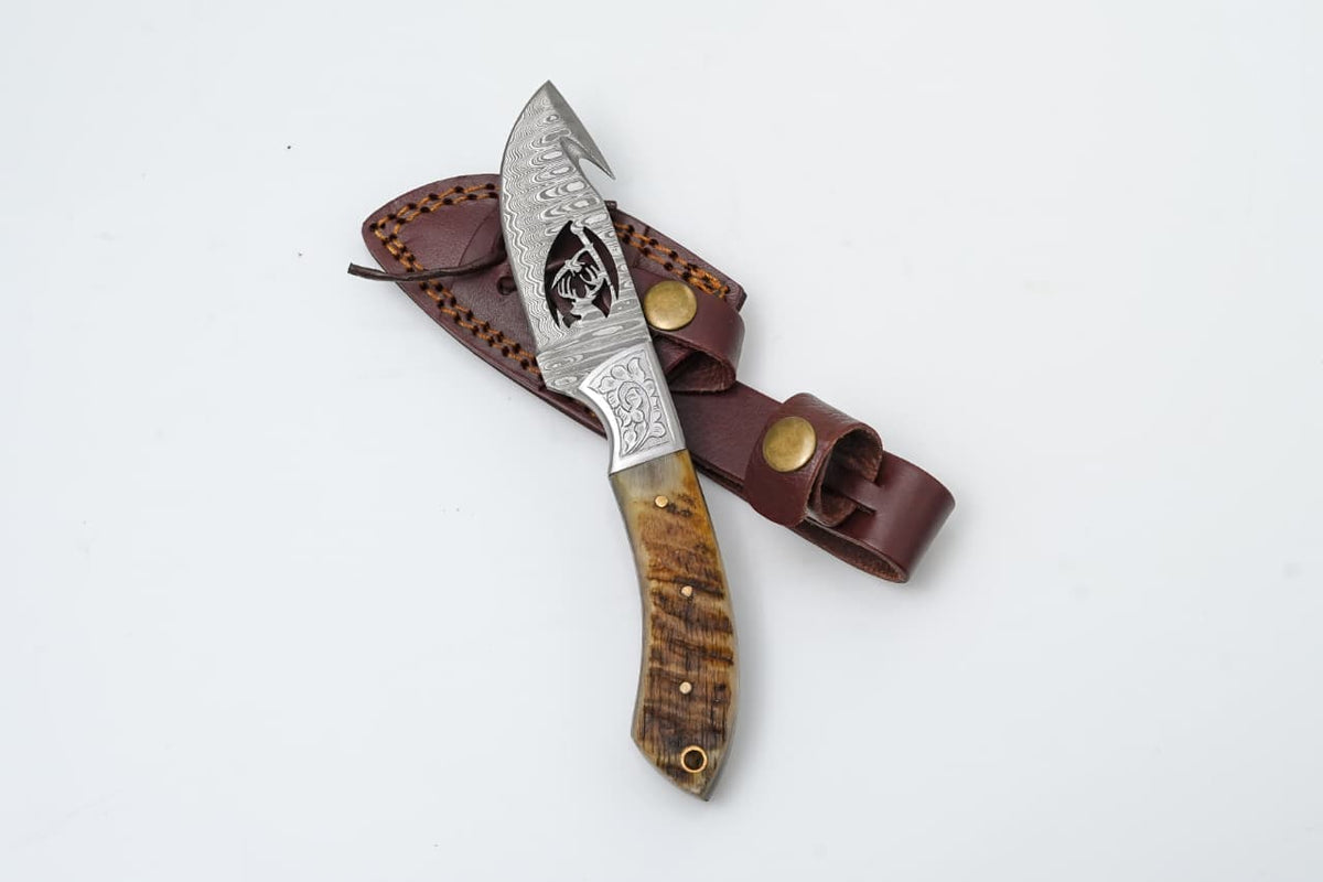 Wire-Cut Damascus Guthook Knife with Ram Horn Handle displayed with leather sheath