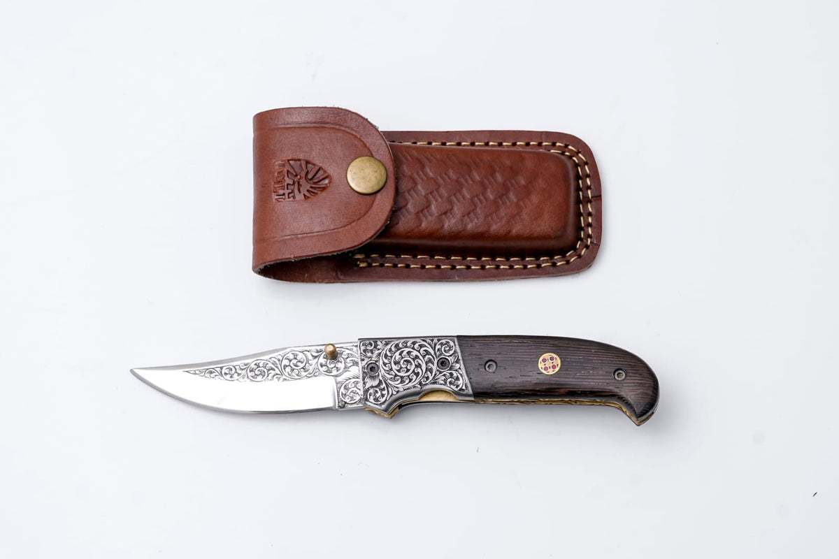 Hand-Engraved Folding Knife TF-092 with detailed blade and wenge wood handle resting beside a leather sheath