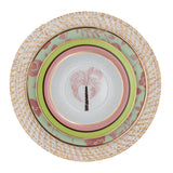 White rattan charger plate with woven texture holding three stacked ceramic plates featuring pastel green, pink, and floral patterns with gold trim and a palm tree motif.